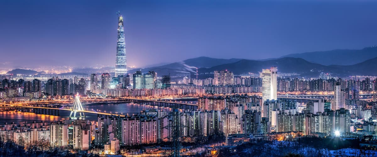 A cityscape at night with a prominent skyscraper, a river, and surrounding high-rise buildings.