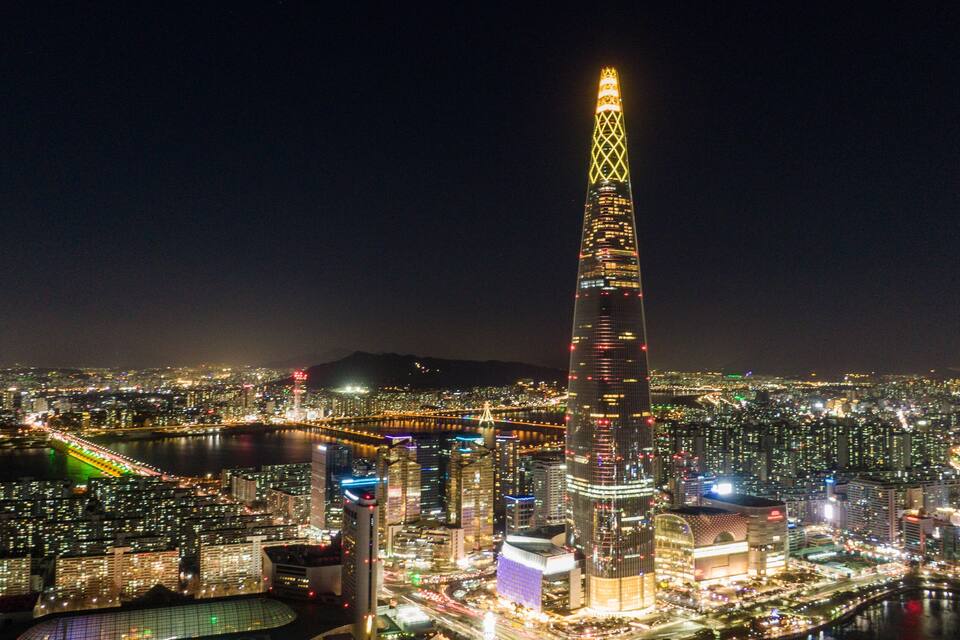 A cityscape at night with a prominent illuminated skyscraper, a river, and surrounding buildings.