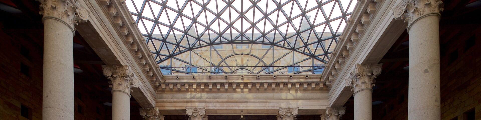 A grand hall with large columns, a glass ceiling, and an arched doorway.