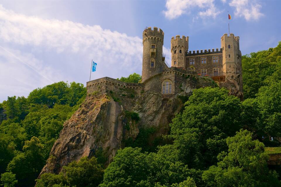 Eine Burg auf einer Klippe, umgeben von üppiger Vegetation.