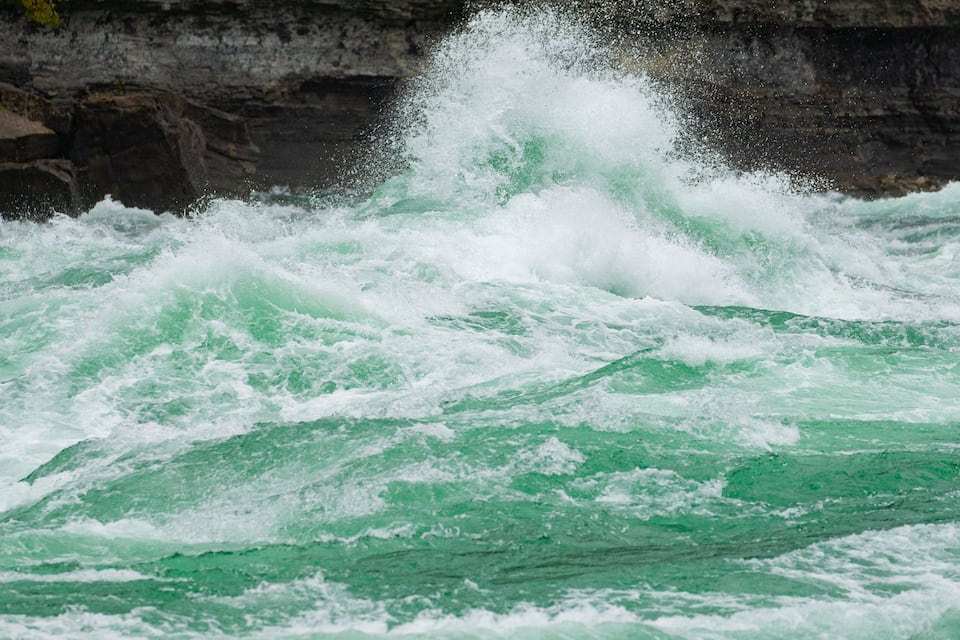Turbulent green water with white foam against a rocky cliff.