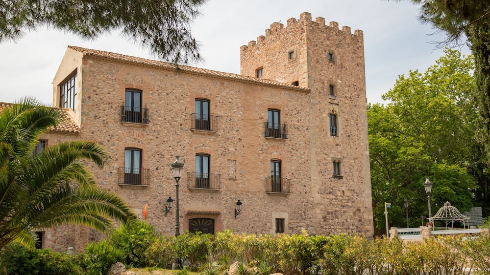 A historic stone building with a tower, surrounded by lush greenery and palm trees.
