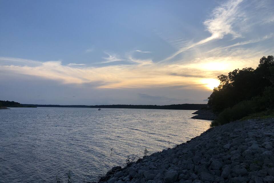A calm lake with a rocky shoreline and a sunset in the background.