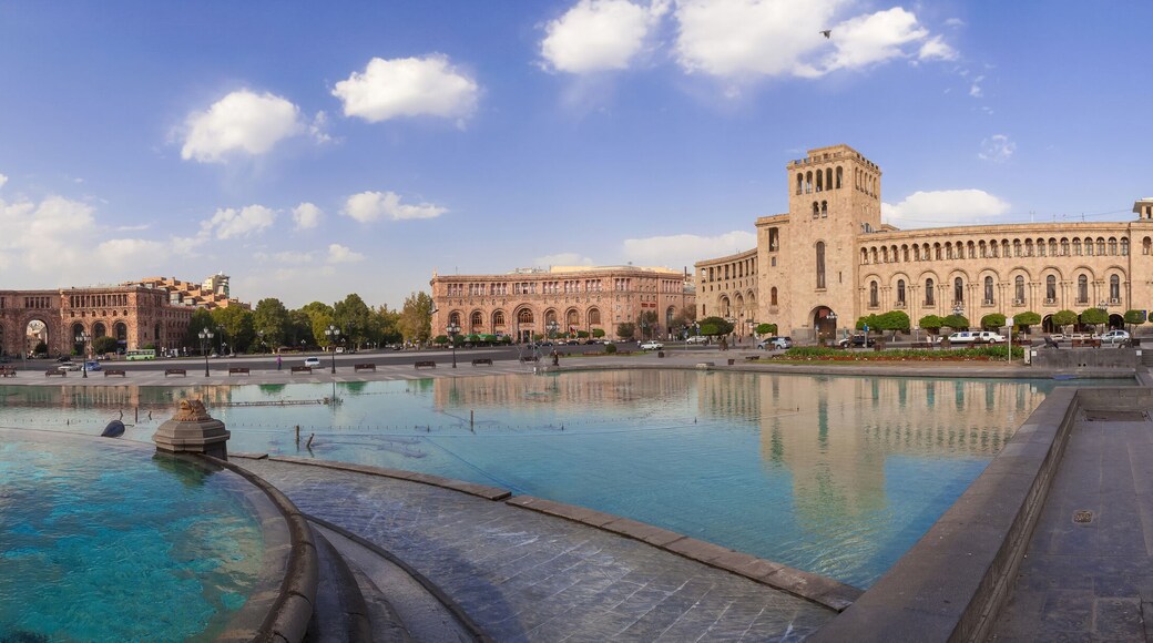 A large public square with a central fountain, historic buildings, and a clear sky.