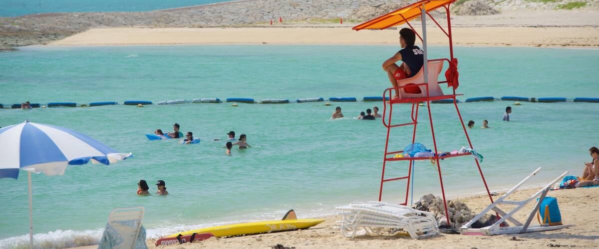 A lifeguard tower with a yellow flag, beach umbrellas, and people swimming in the ocean.