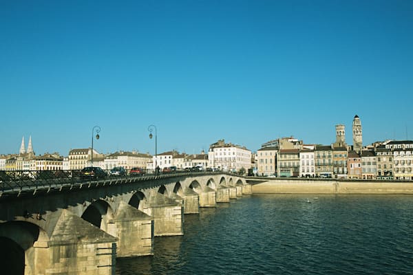 Un pont de pierre enjambant une rivière, avec des bâtiments et des tours en arrière-plan.