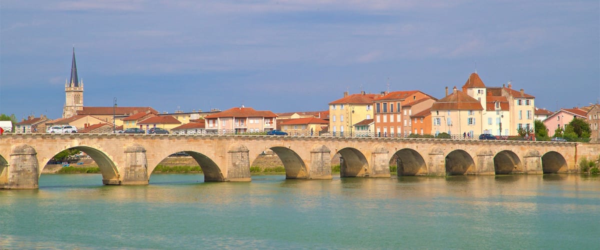 A stone bridge with multiple arches spanning a river, with buildings and a church in the background.