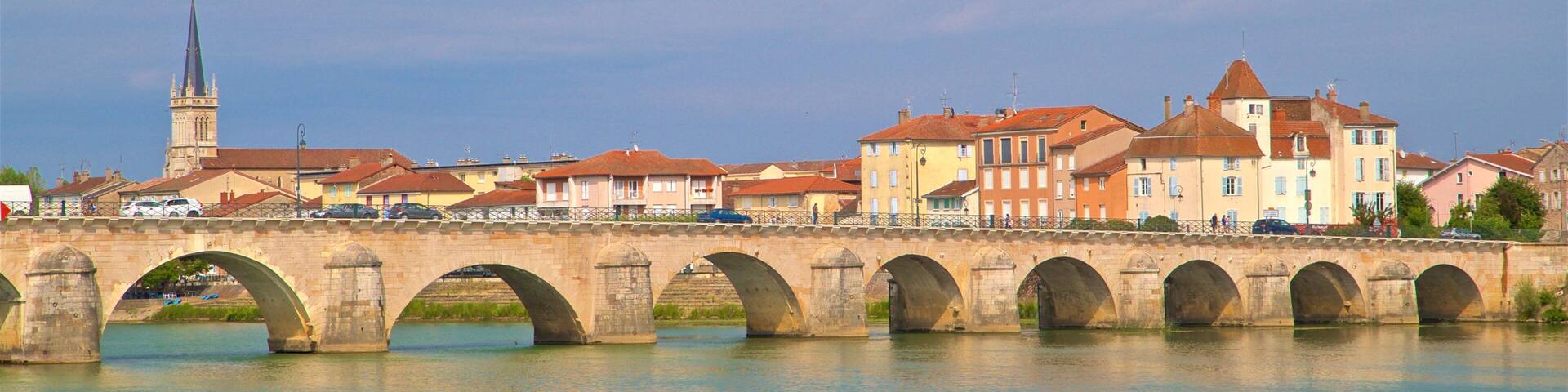 A stone bridge with multiple arches spanning a river, with buildings and a church in the background.