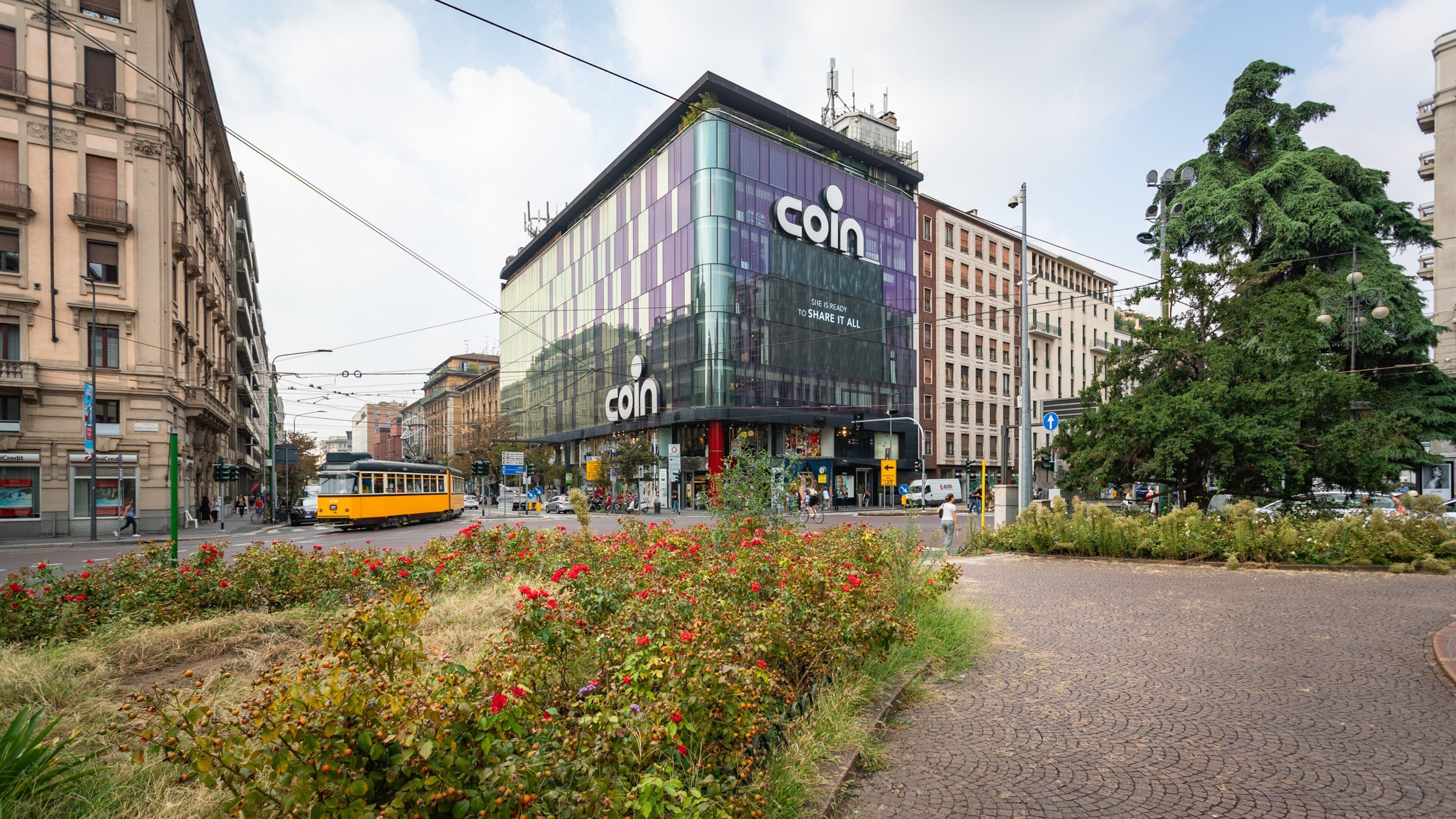 A modern building with a large 'coin' sign, surrounded by urban streets and greenery.