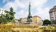 A monument with a tall obelisk, surrounded by colorful flowers and classic buildings.