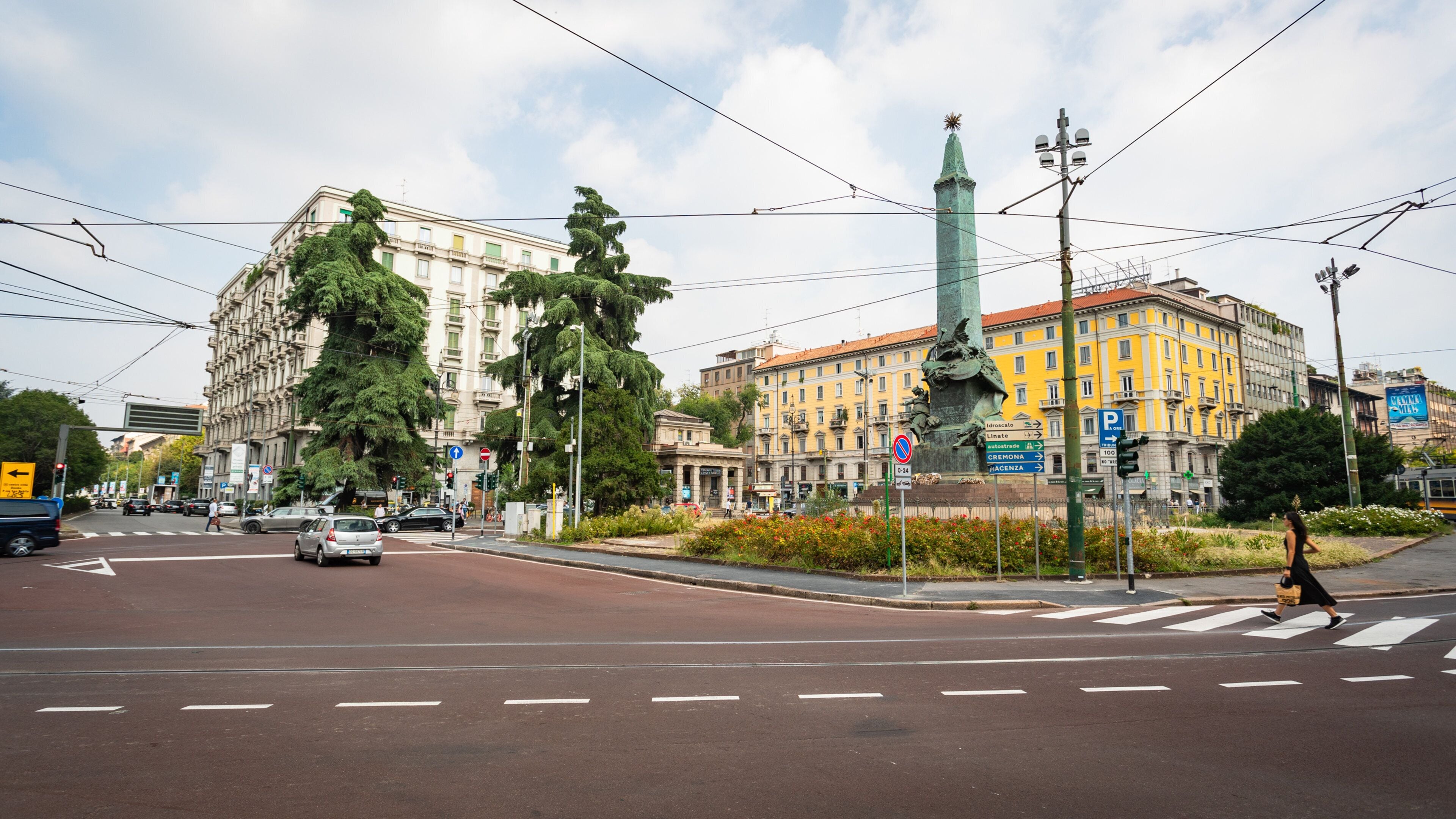 A city intersection with traffic lights, a tram, and a statue.