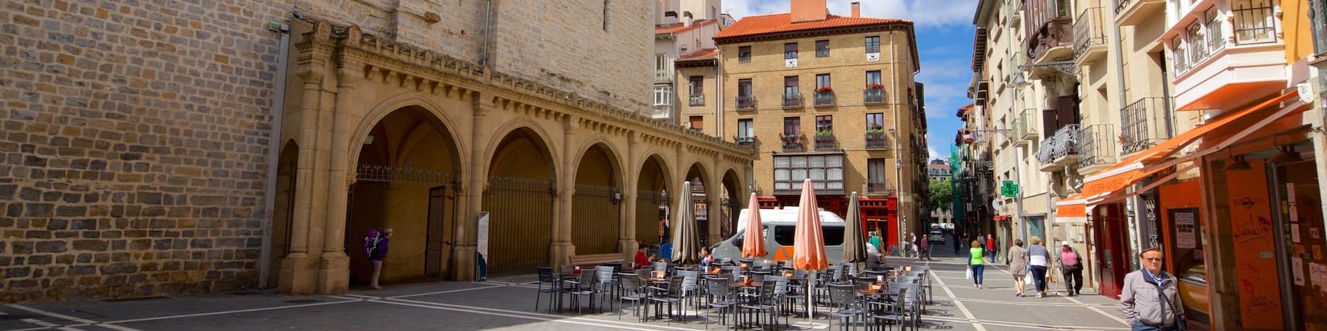 A historic square with stone buildings, a clock tower, and outdoor seating areas.