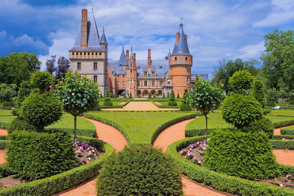 Un château historique doté de nombreuses tours, un jardin magnifiquement entretenu et un ciel d’un bleu éclatant.