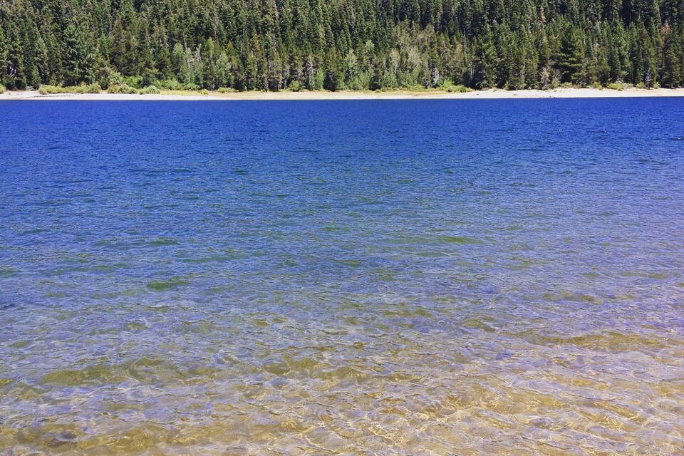 Un lago cristalino con una colina boscosa al fondo.