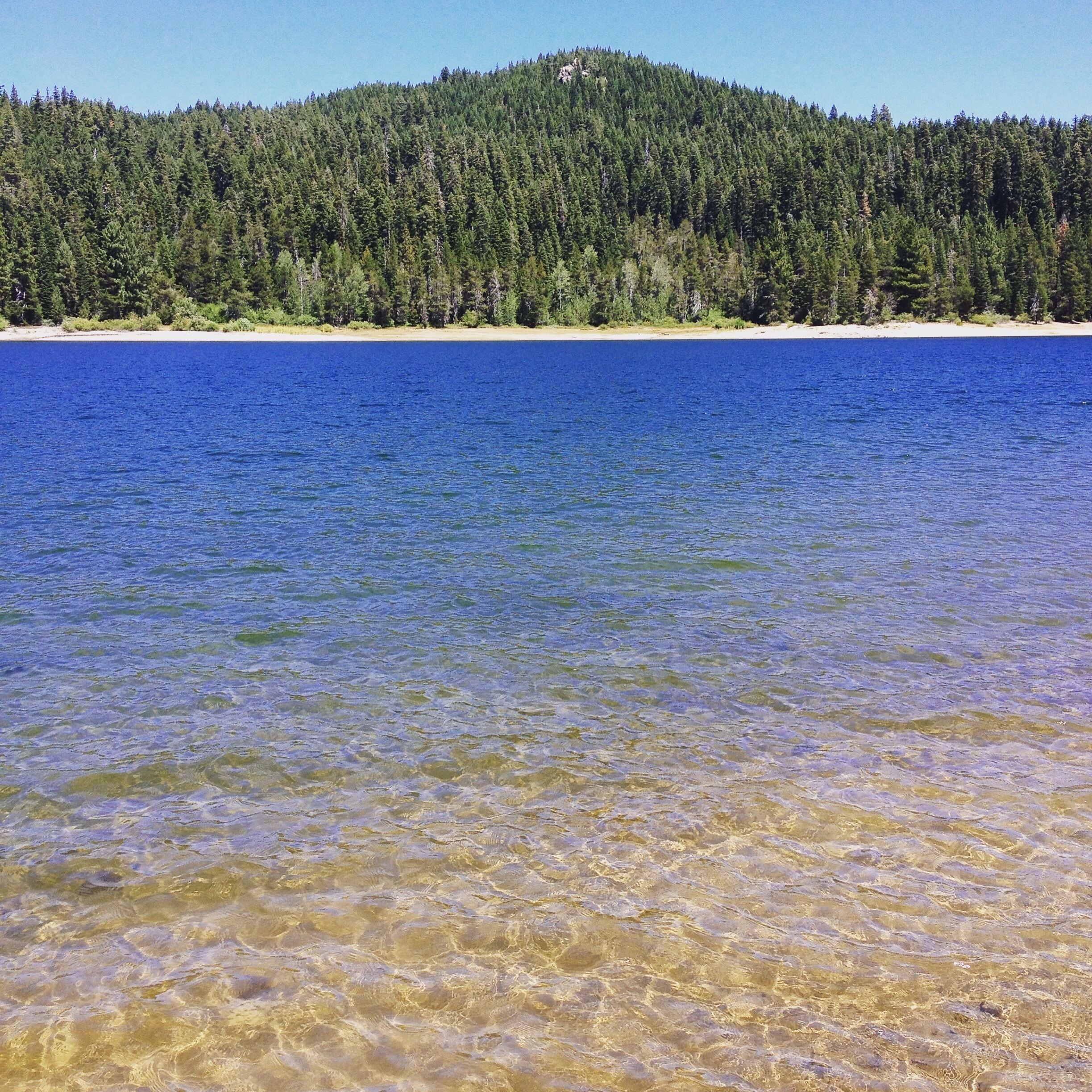 A clear lake with a forested hill in the background.