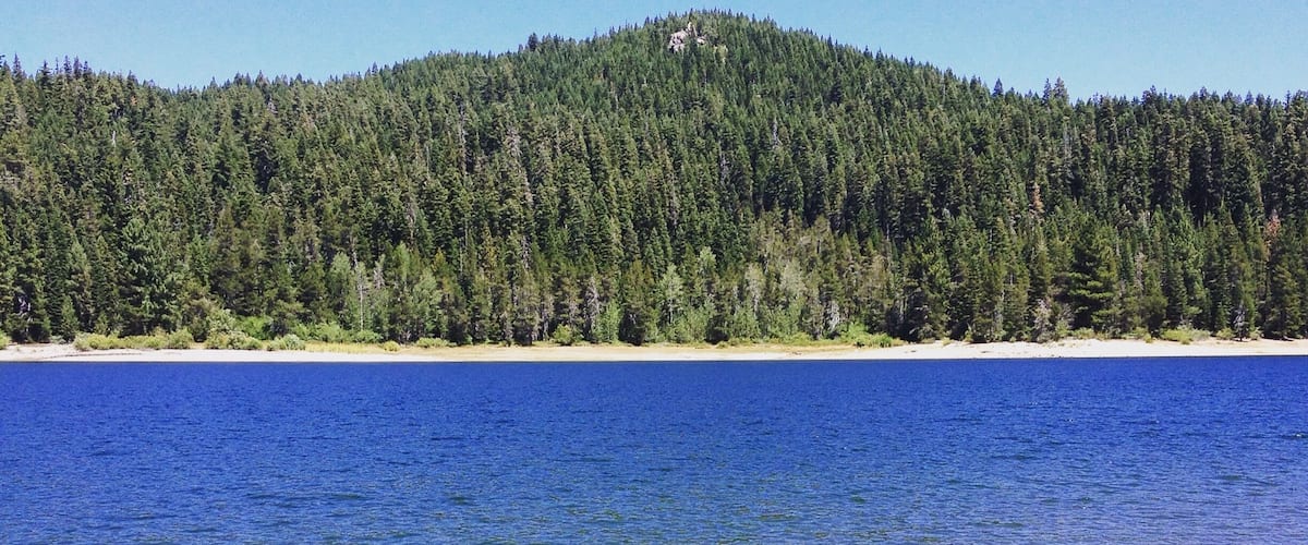 A clear lake with a forested hill in the background.