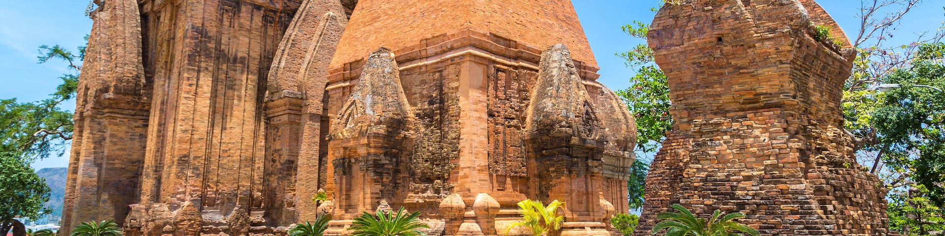 A large, ancient brick temple with a central pyramid-like structure, surrounded by smaller buildings and potted plants.