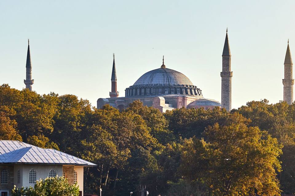 A mosque with a large dome and four minarets, surrounded by trees.