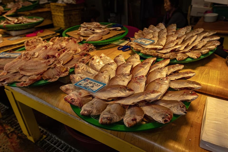 A variety of dried fish displayed on green plates at a market.