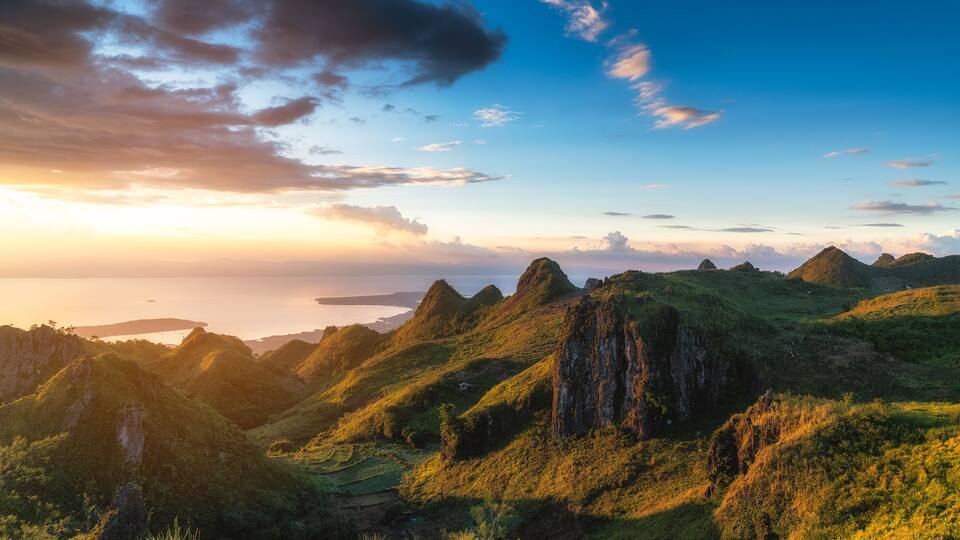 A mountainous landscape with green hills and rocky outcrops during sunset.