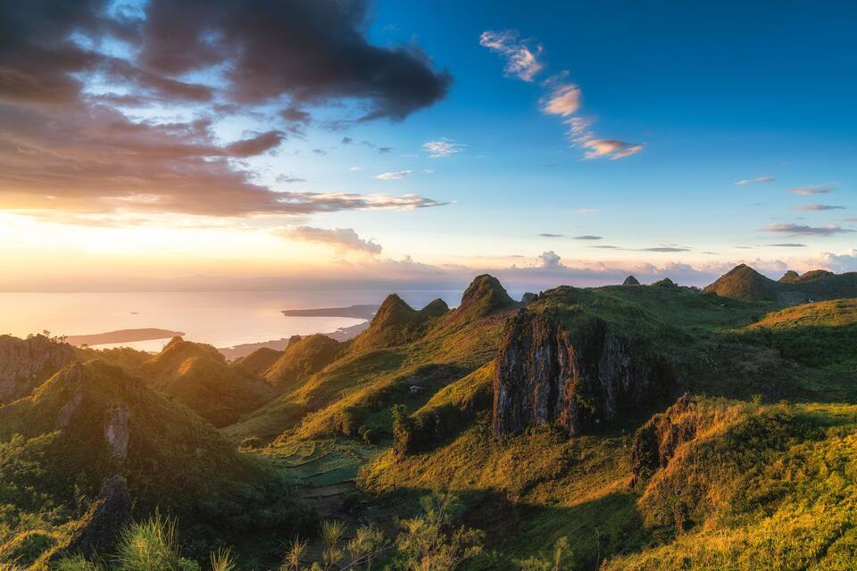 A mountainous landscape with green hills and rocky outcrops during sunset.