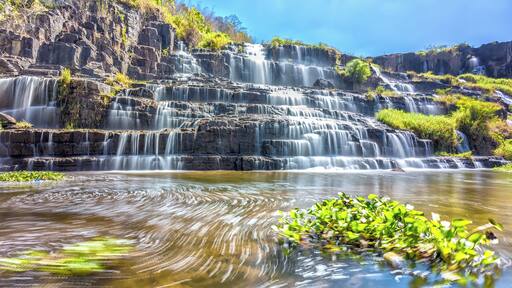 Ponguor Waterfall in the sun with water flowing down the stairs step by creating its folds like silk, beneath the swirl of all scraped up the beauty of nature in Lam Dong, Vietnam