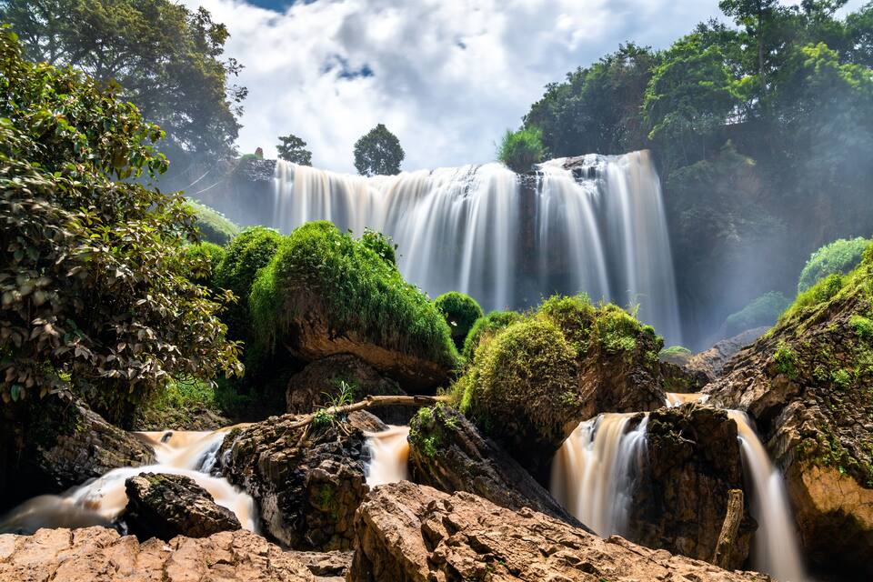 Een waterval omgeven door weelderige begroeiing en rotsen begroeid met mos.