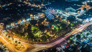 Vista aérea de una ciudad de noche con una noria destacada, calles iluminadas y una glorieta.