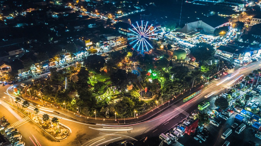 Vista aérea de una ciudad de noche con una noria destacada, calles iluminadas y una glorieta.