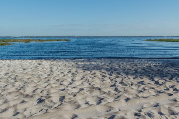 Uma praia de areia com mar azul calmo e costa distante.