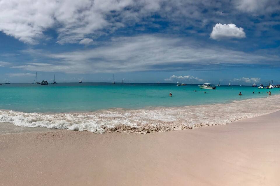 Uma praia com águas azul-turquesa, barcos e céu claro.