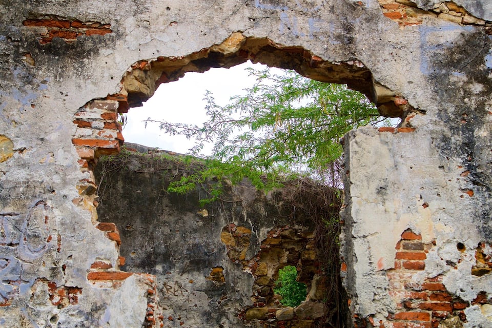 An ancient, weathered stone archway with visible brickwork and vegetation growing through the cracks.