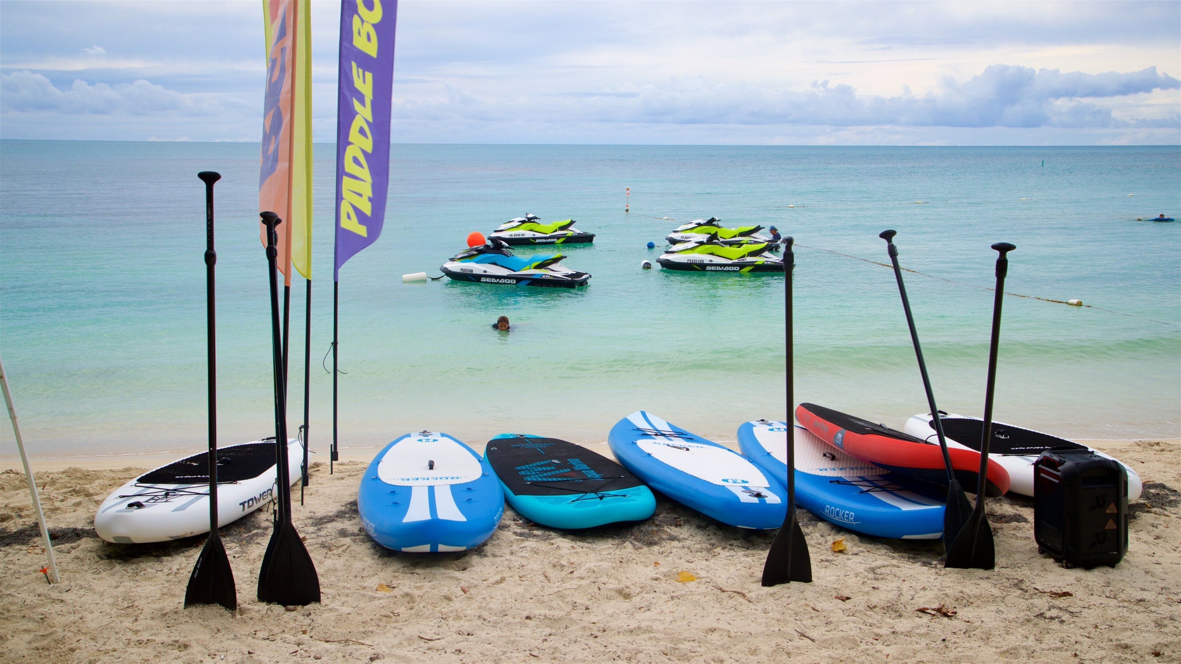 Paddleboards, kayaks, and a flag on a beach with the ocean in the background.