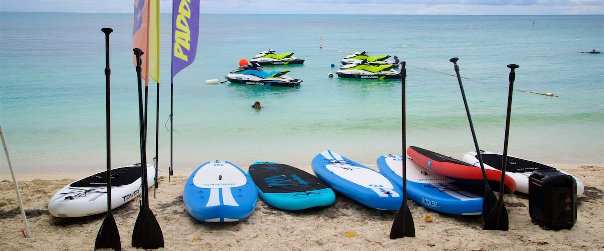 Paddleboards, kayaks, and a flag on a beach with the ocean in the background.