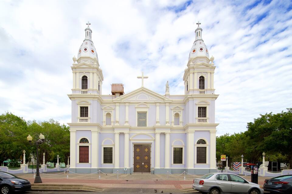 A white church with two towers and a central dome, surrounded by trees and parked cars.