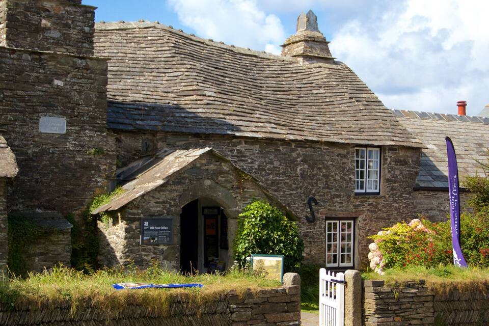 A stone building with a thatched roof, a sign reading "Old Post Office," and a purple flag.