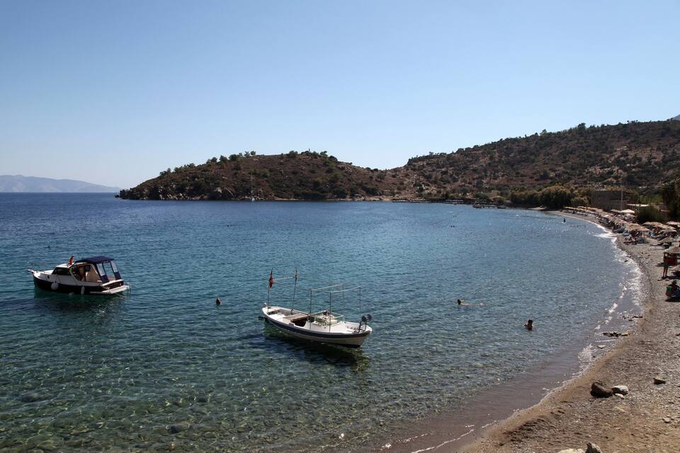 Une vue dégagée sur la côte, avec des bateaux sur une eau calme, une plage de sable et un paysage vallonné en arrière-plan.