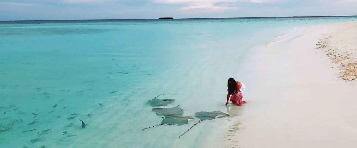 A beach with clear turquoise water and a person in a red dress walking along the shore.
