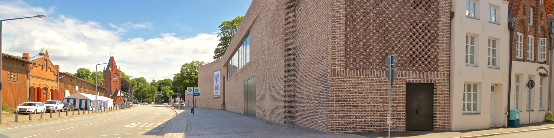 Un edificio moderno con una fachada triangular singular y un edificio de ladrillo tradicional cercano.