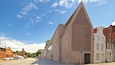 A modern building with a unique triangular facade and a traditional brick building nearby.
