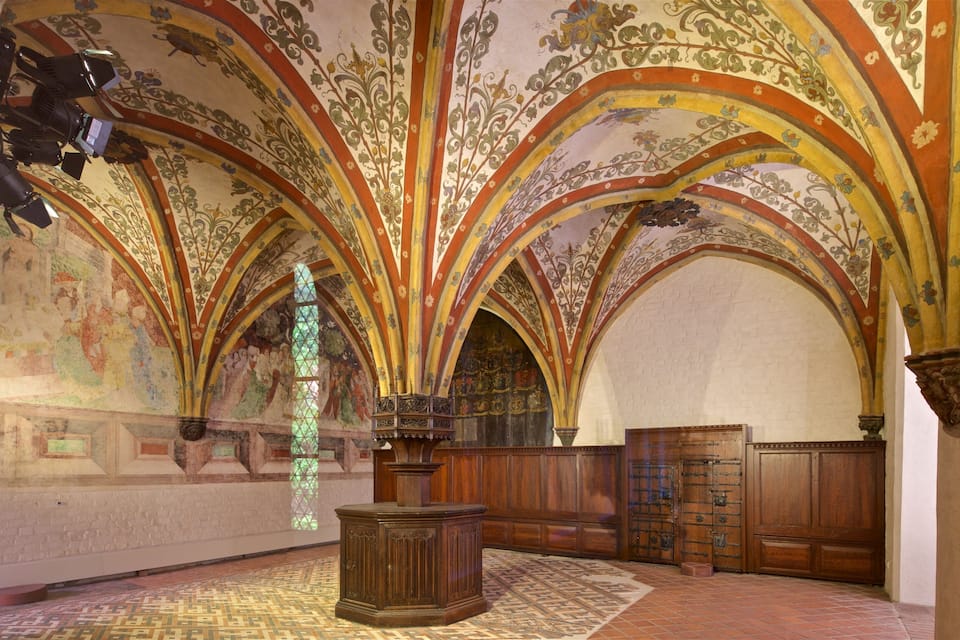 A richly decorated hall with arched ceilings, intricate floral patterns, and wooden furniture.