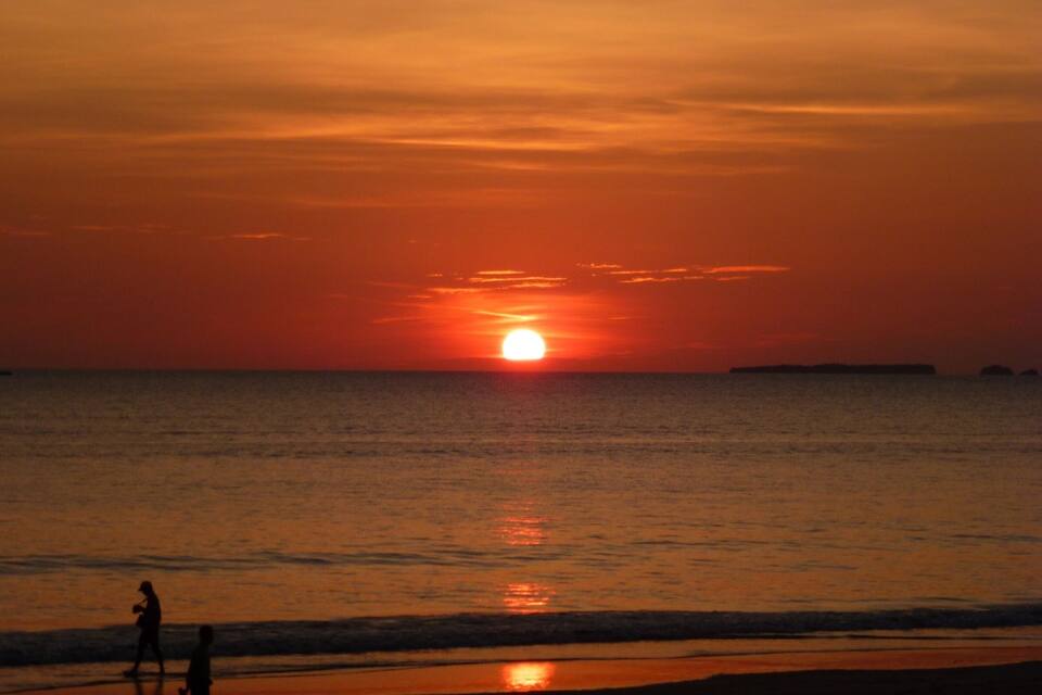 Tramonto sull'oceano con le sagome di persone sulla spiaggia.