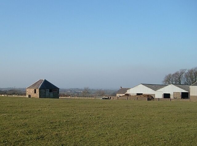 A rural landscape with a grassy field, a small stone building, and several white barns.