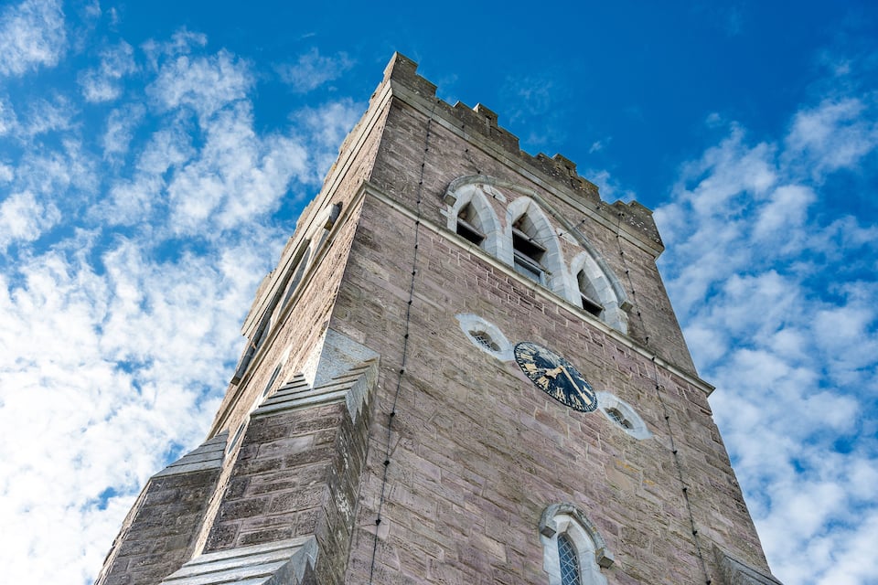 A tall brick tower with a clock and arched windows against a blue sky with clouds.