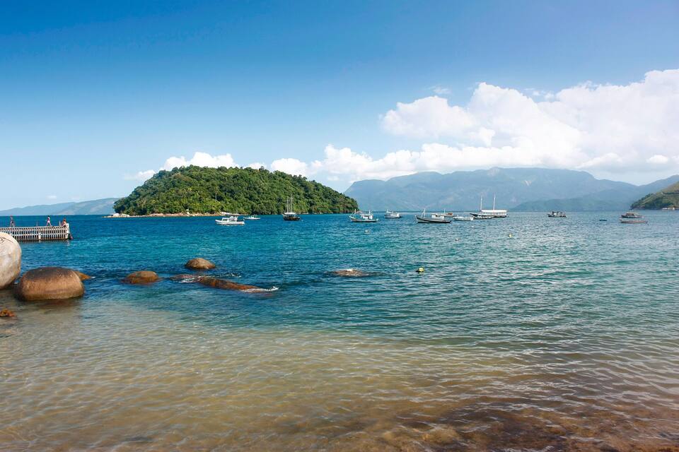 A clear lake with boats, a rocky shore, and a forested island in the background.