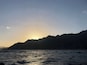 A sunset over a mountainous coastline with rough sea waves.