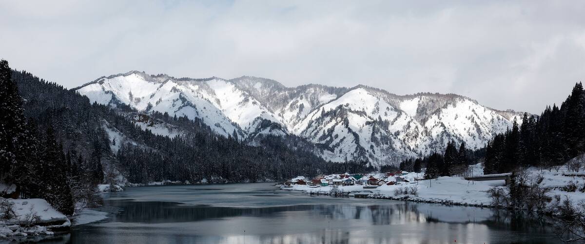 A snow-covered mountain range, a frozen lake, and a small settlement with buildings.
