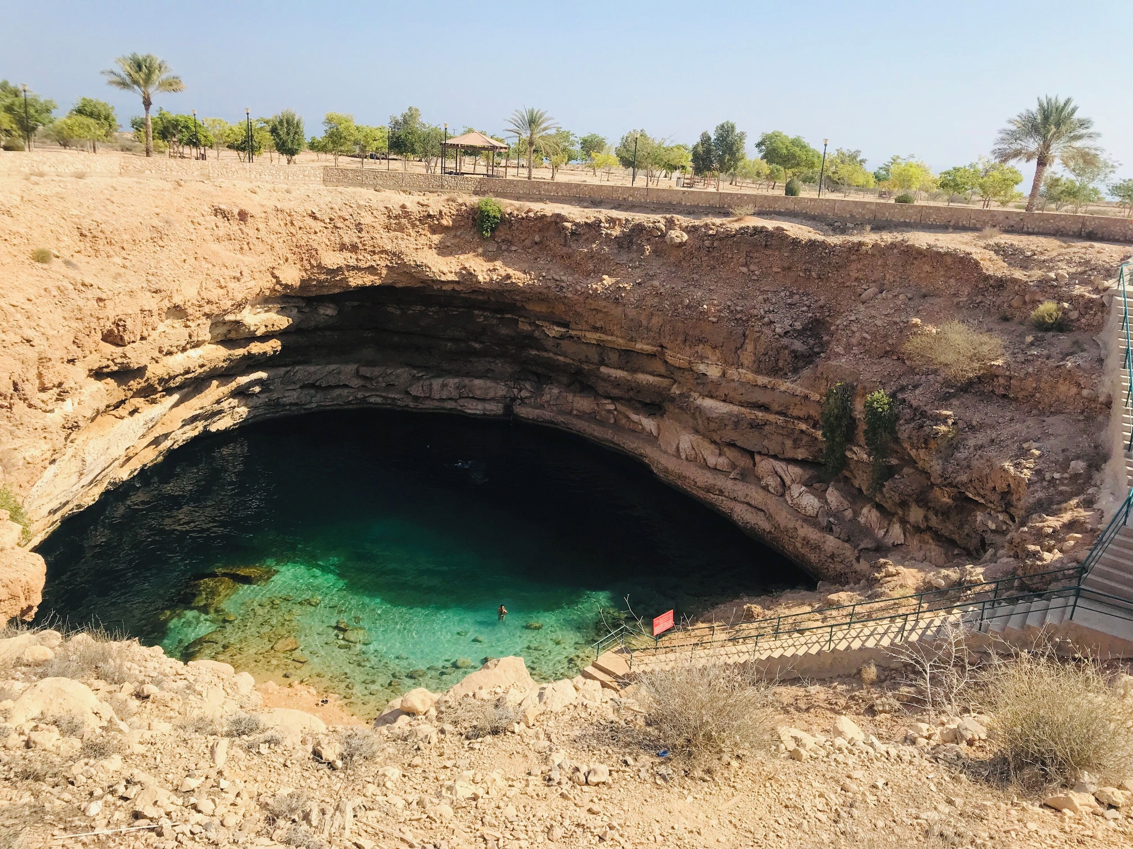 A natural cave opening with clear water, surrounded by rocky terrain and sparse vegetation.