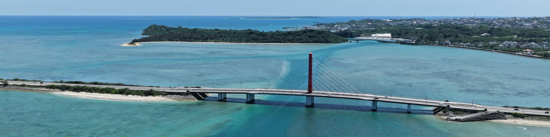 A bridge spanning a clear blue sea with a coastal town in the background.