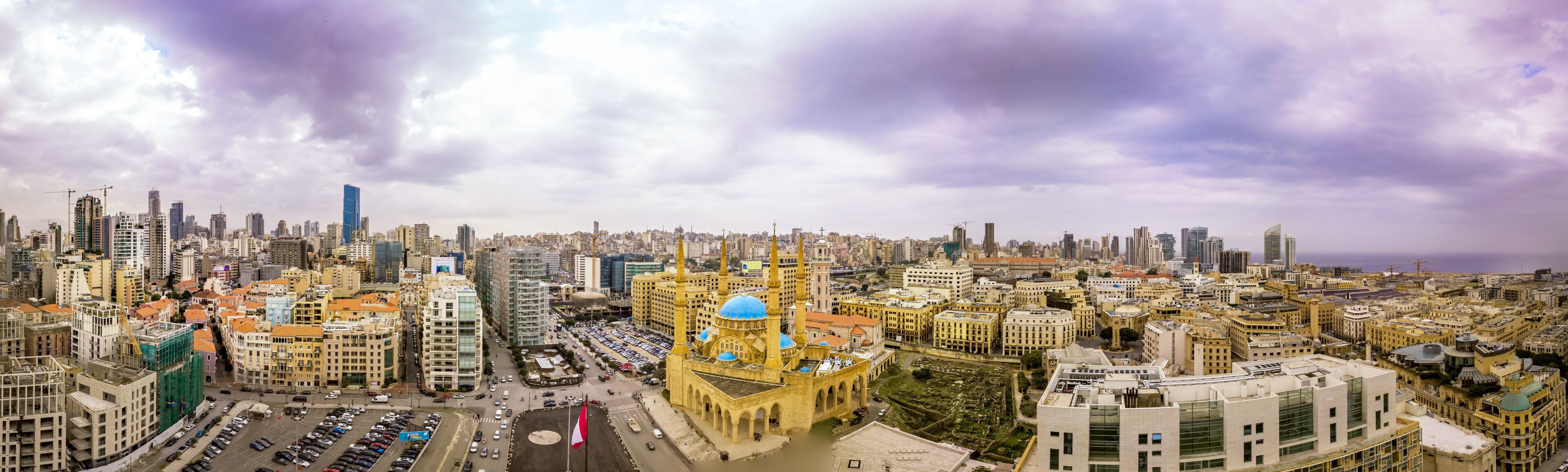 A cityscape with a prominent mosque featuring a blue dome, surrounded by modern and historical buildings.
